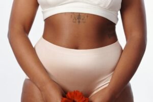 An Image of a black woman in plain underwear placing a red flower in front of her vagina