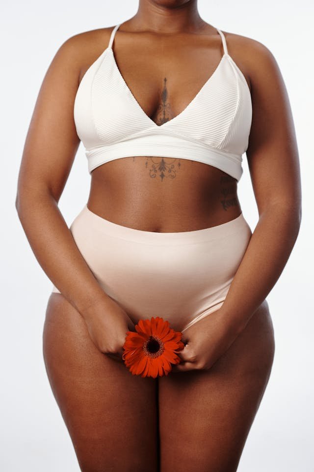 An Image of a black woman in plain underwear placing a red flower in front of her vagina