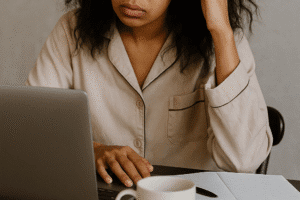 AI Inage A dishevelled woman in pyjamas on a laptop surrounded by notebooks—caption: “CEO, COO, Caffeine Dependent”