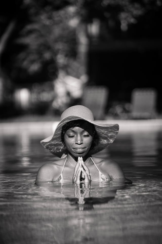 A black and white image of a black woman putting her hands together in a prayer position in a body of water