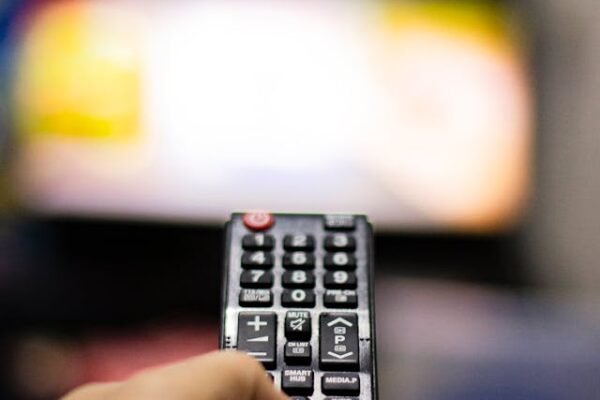 A man's hand holding a remote control aimed at the blurred out tv image