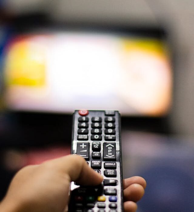 A man's hand holding a remote control aimed at the blurred out tv image