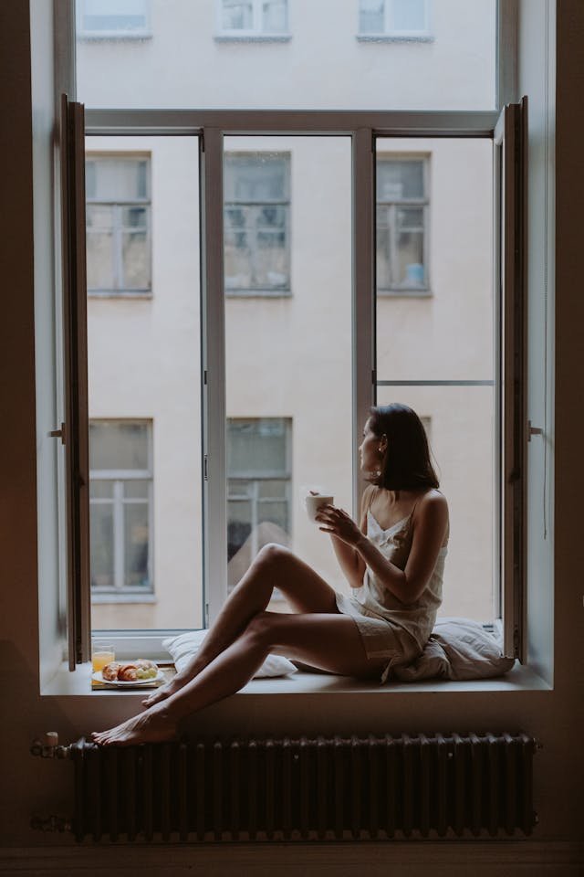 An Image of a woman looking out a window, symbolising reflection and late awakening.