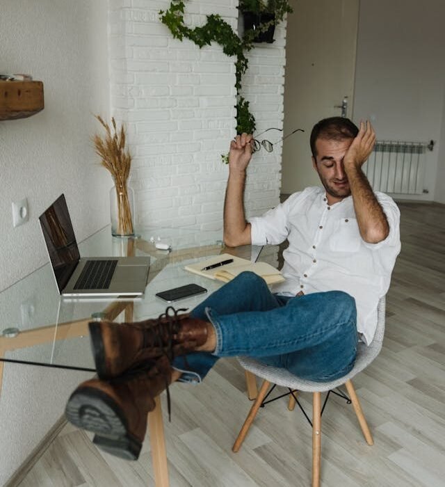 A man sitting at his home desk looking tired and rubbing his eyes