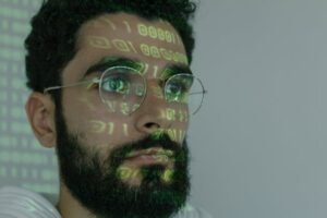 A man sitting in front of a computer screen with the reflection of code on his face.