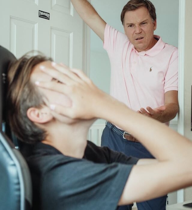 A woman sat with her hands over her face frustrated with a man looking at her in confusion