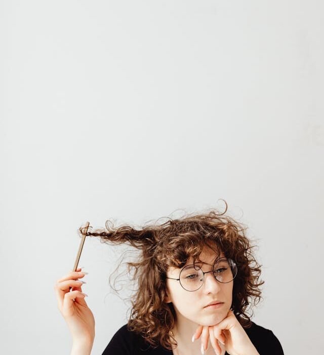 I woman staring outward twirling her hair with a pencil creating a mindless knot