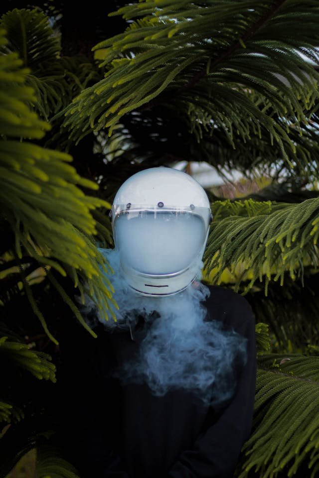 A person hiding in the bushes with a helmet on filled with smoke to represent brain fog.