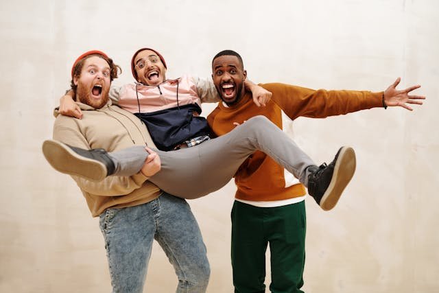A mulitcultral group of 3 men, with 2 lifting the man in the middle up and them all smiling and laughing