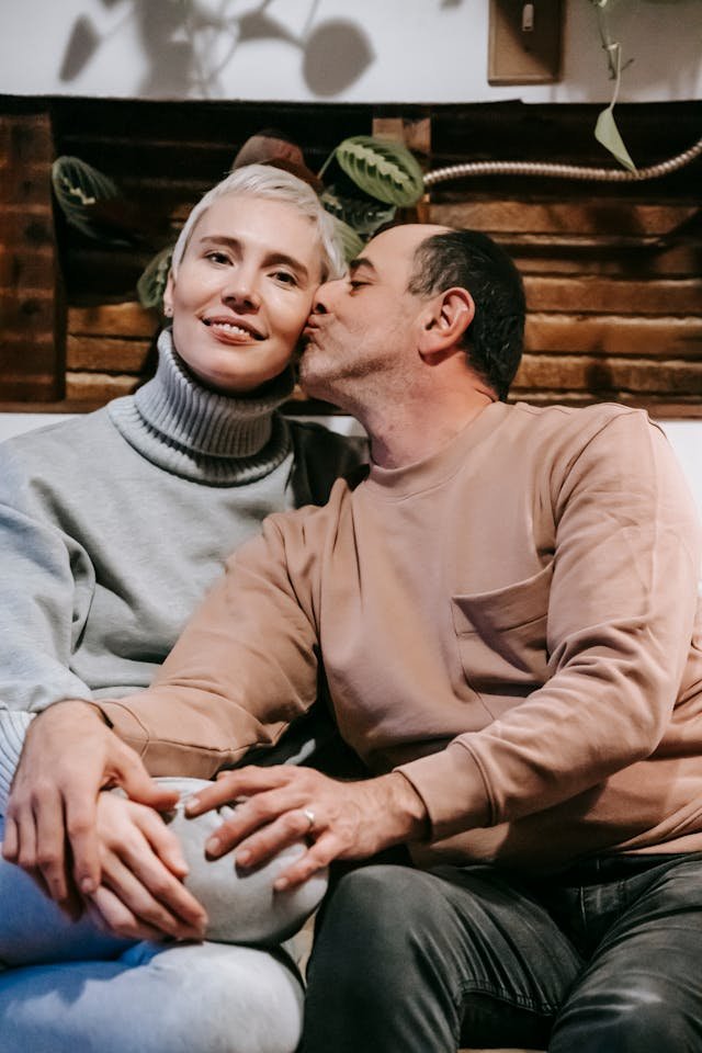 A man giving his partner a kiss on the cheek and her smiling in adoration