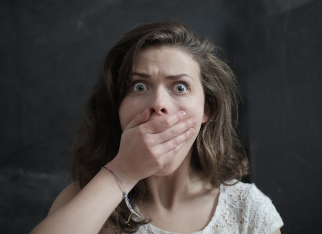 A woman looking shocked covering her hand over her mouth in shock 