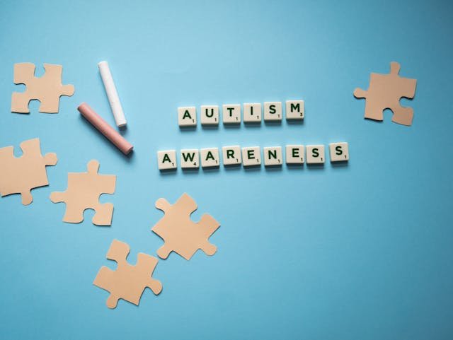 An Image of A slogan of autism awareness spelled on scrabble tiles with a light bulb drawing
