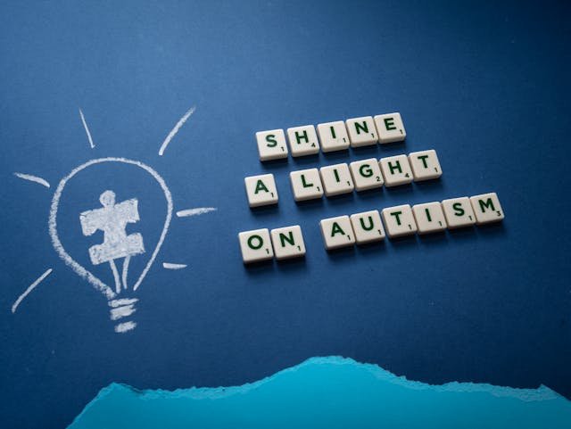 An Image of A slogan of Shine a light on autism spelled on scrabble tiles with a light bulb drawing