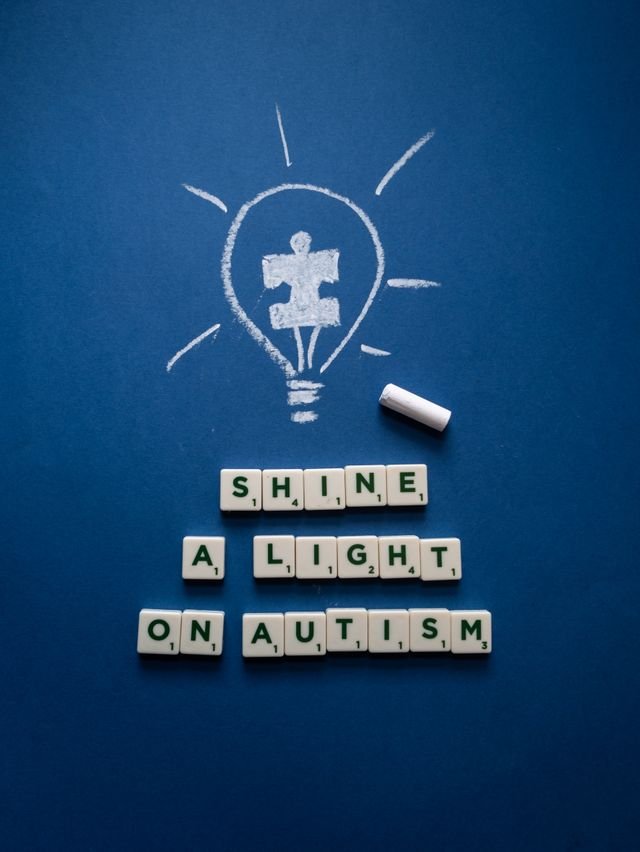 A blue poster with a lightbulb drawn witha puzzle piece inside. The words Shine a light on Autism in scrabble tiles
