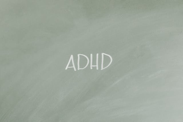 The letters ADHD written in white chalk on a greyish -green background