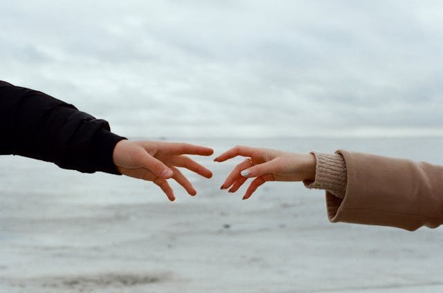An image of a female and a male hand reaching for each other but not quite able to connect