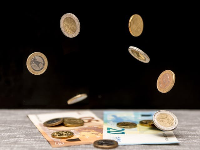 Image of free falling euro coins landing on euro notes on a black background