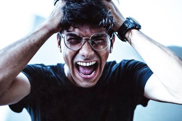 A man screaming out with his hands resting on his head in despair
