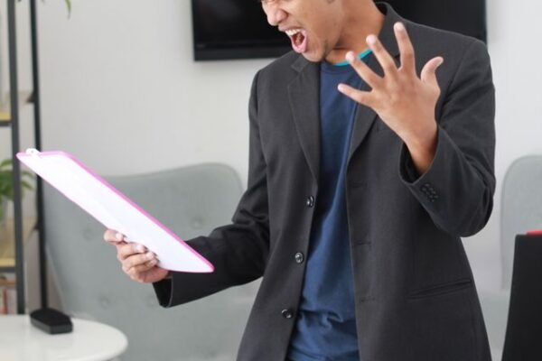 A man in a black suit holiding a paper looking angry