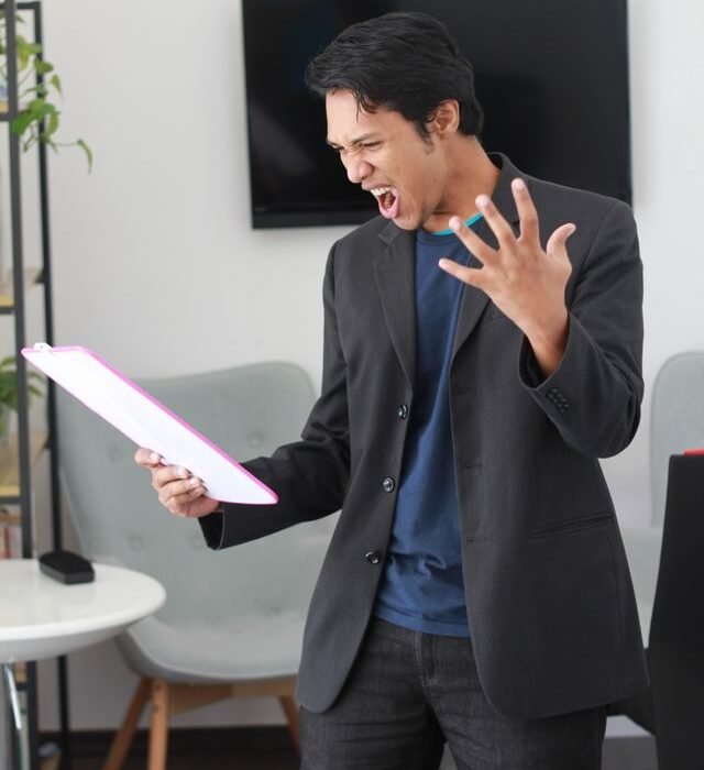 A man in a black suit holiding a paper looking angry