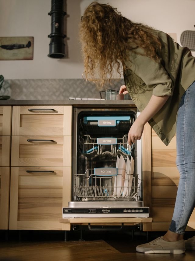 A woman bending over loading a dishwasher
