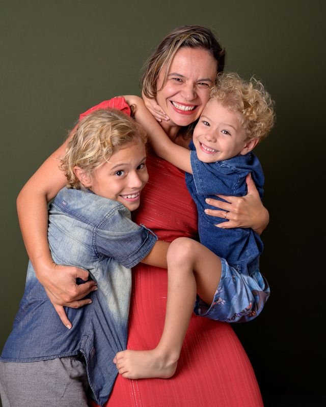 A mother cuddling her 2 boys one older and the other a toddler, all smiling and happy