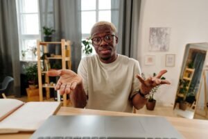 A man sitting at a desk looking clueless with his palms showing with the expression he has no clue