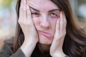 A woman holding boths sides of her face one side being pulled up the other pulled down