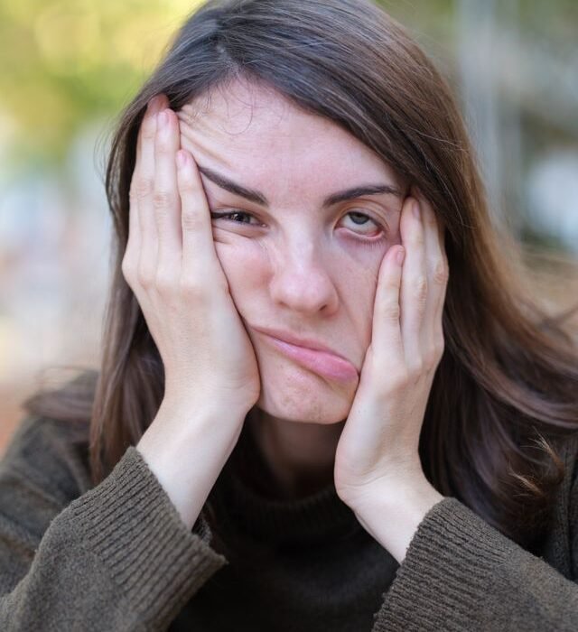 A woman holding boths sides of her face one side being pulled up the other pulled down
