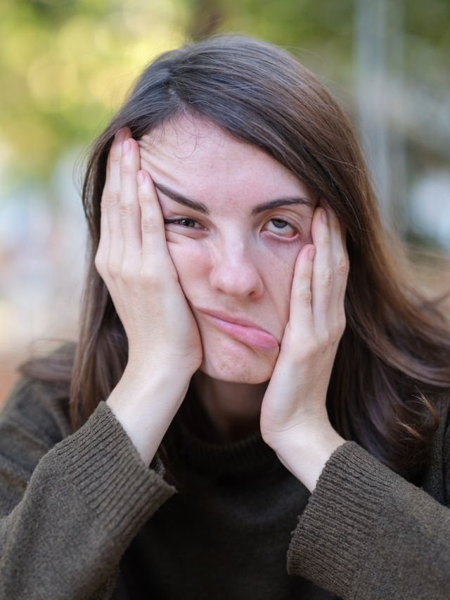 A woman holding boths sides of her face one side being pulled up the other pulled down