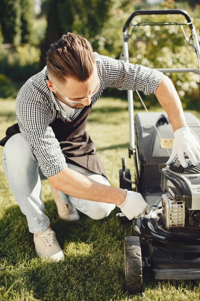 A man on one knee fixing a lawnmower