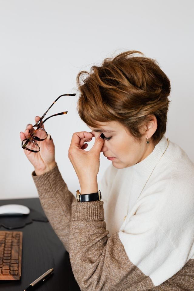 A woman pinching the bridge of her nose whilst holding her glasses with her other hand