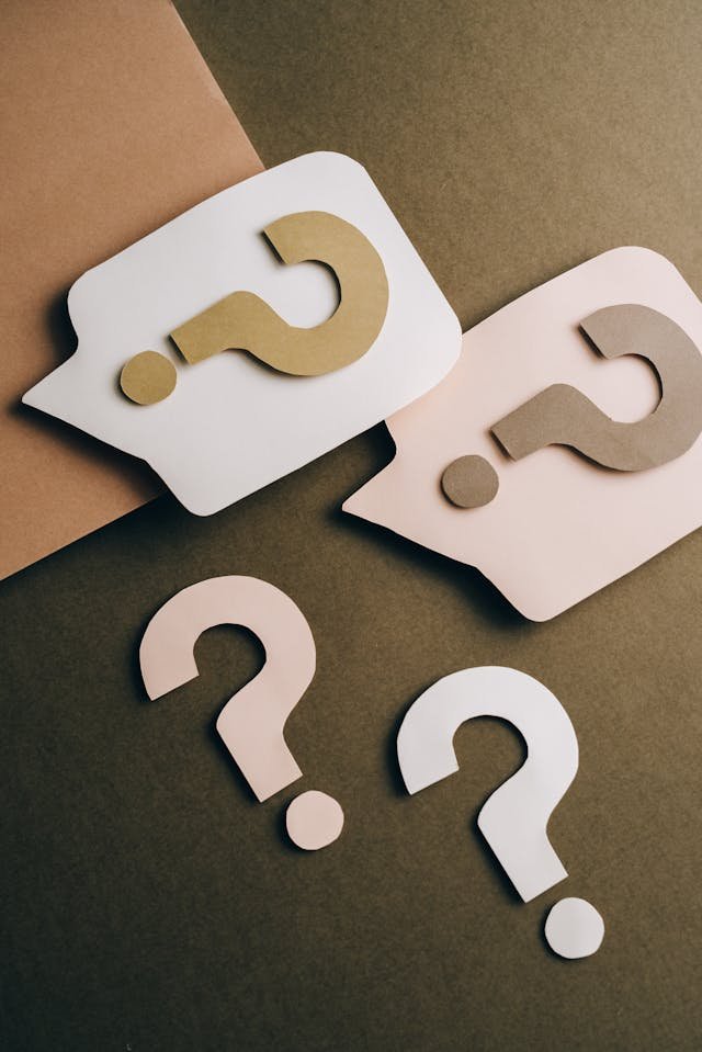 Several neutral coloured cutouts of question marks on a brown background