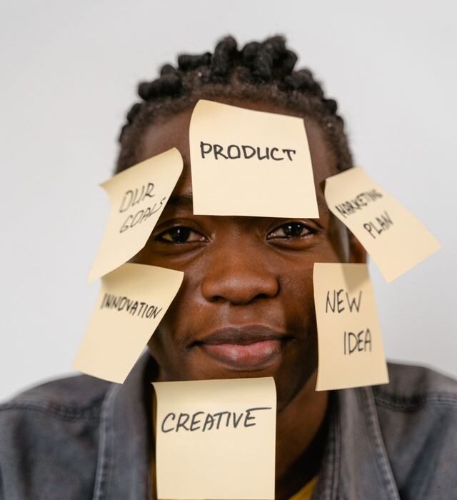 A man with various sticky notes over his face with different words like Product, Creative, New Idea