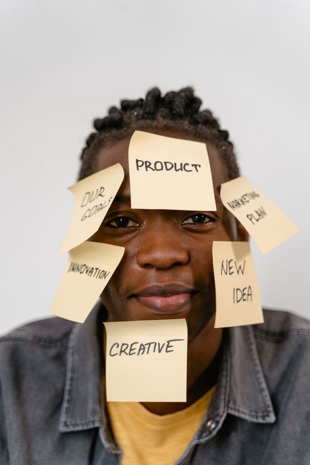 A man with various sticky notes over his face with different words like Product, Creative, New Idea