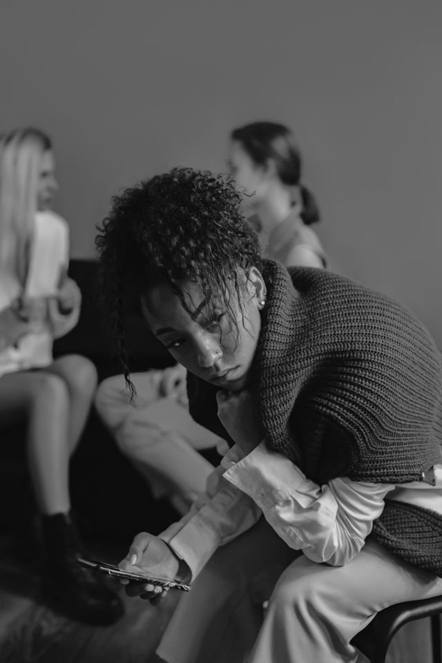 A woman deep in contemplation holding a phone and people in the background talking