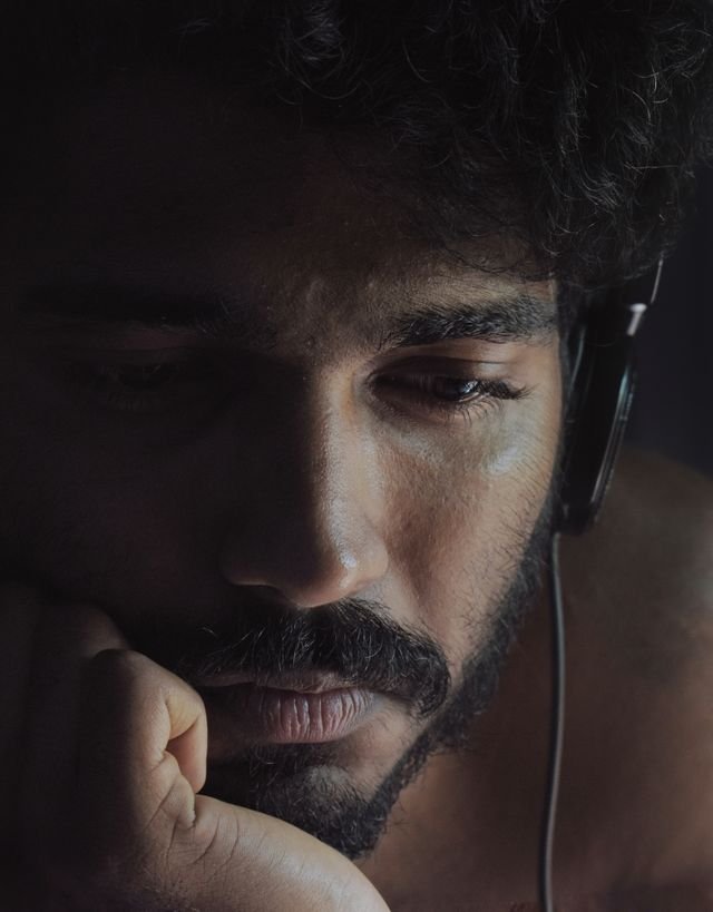 A close up image of a man wearing headphones and looking sad