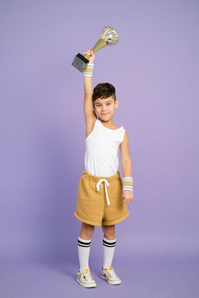 A young boy dressed in sportswear holding up a trophy 