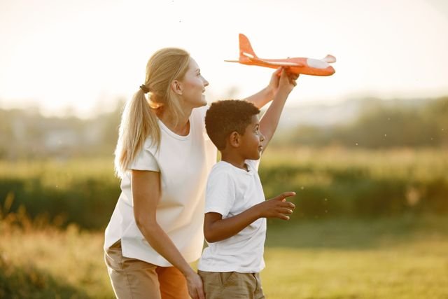 A mother and child in a field and the child posing flying a toy plane
