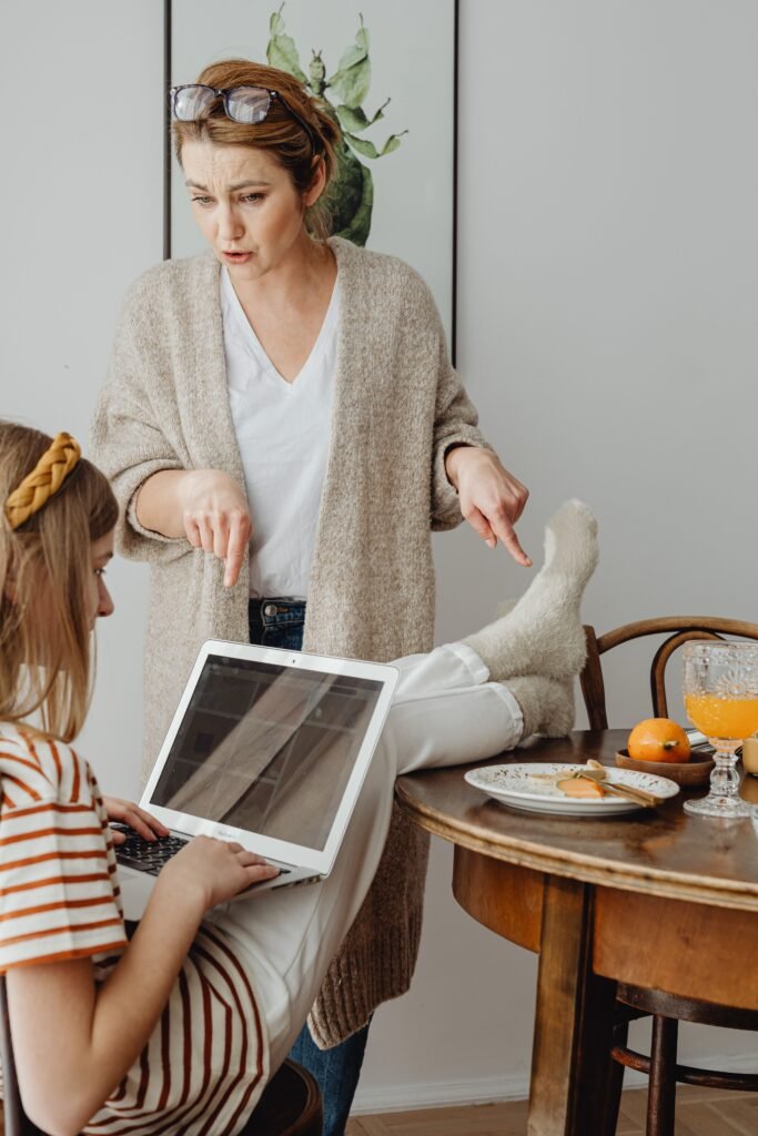 A mother scolding her daughter for using her tablet at the breakfast table whilst propping her feet up at the table too.